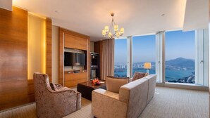 Une chambre d’hôtel moderne dotée d’une grande fenêtre offrant une vue sur la ville et les montagnes, d’un téléviseur à écran plat, d’un minibar et d’un coin salon agrémenté d’un tapis à motifs.