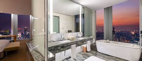 A modern bathroom with a large mirror, two sinks, a bathtub, and a city view.