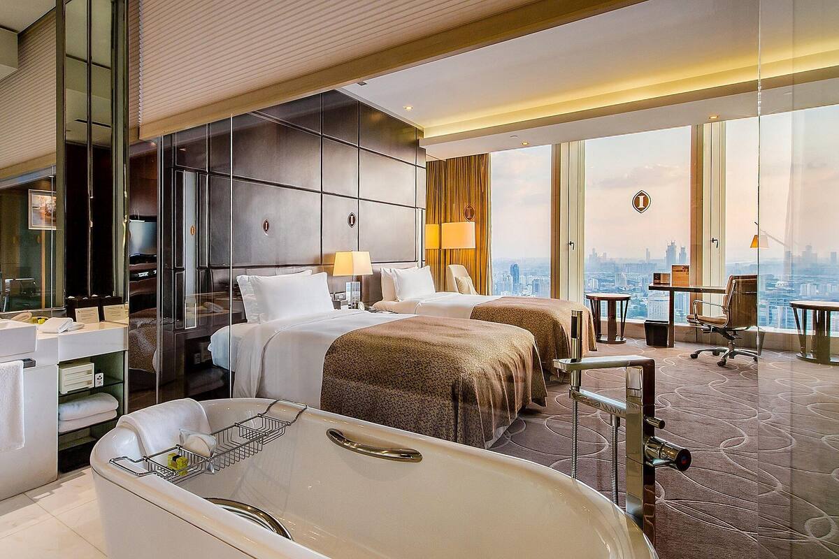 Quarto de hotel com uma banheira grande, duas camas, uma escrivaninha e vista para a cidade.