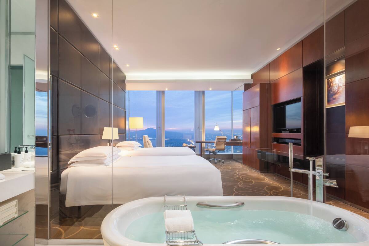 Quarto de hotel com cama grande, área de estar separada, banheira e televisão.