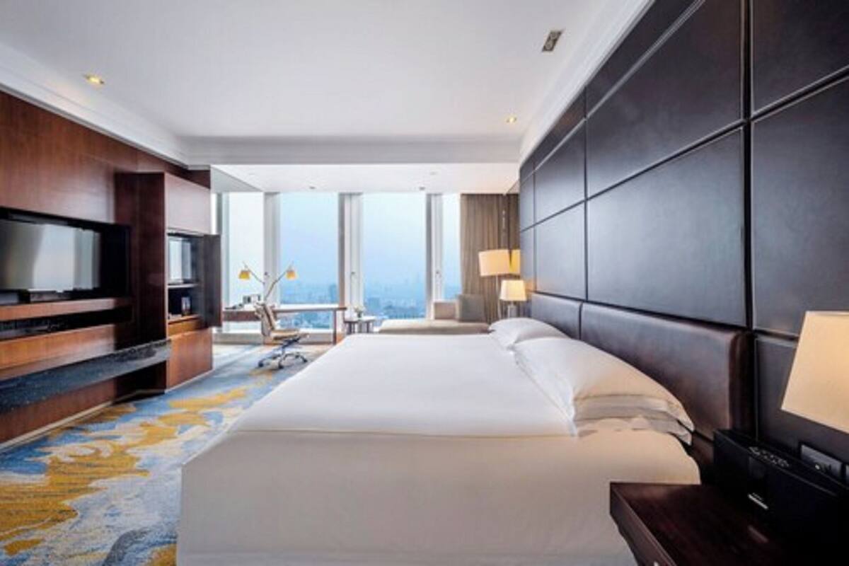 Quarto de hotel moderno com uma cama grande, televisão de tela plana, escrivaninha com cadeira e vista para a cidade.