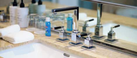 A bathroom sink with multiple faucets, a mirror, and various toiletries on the countertop.