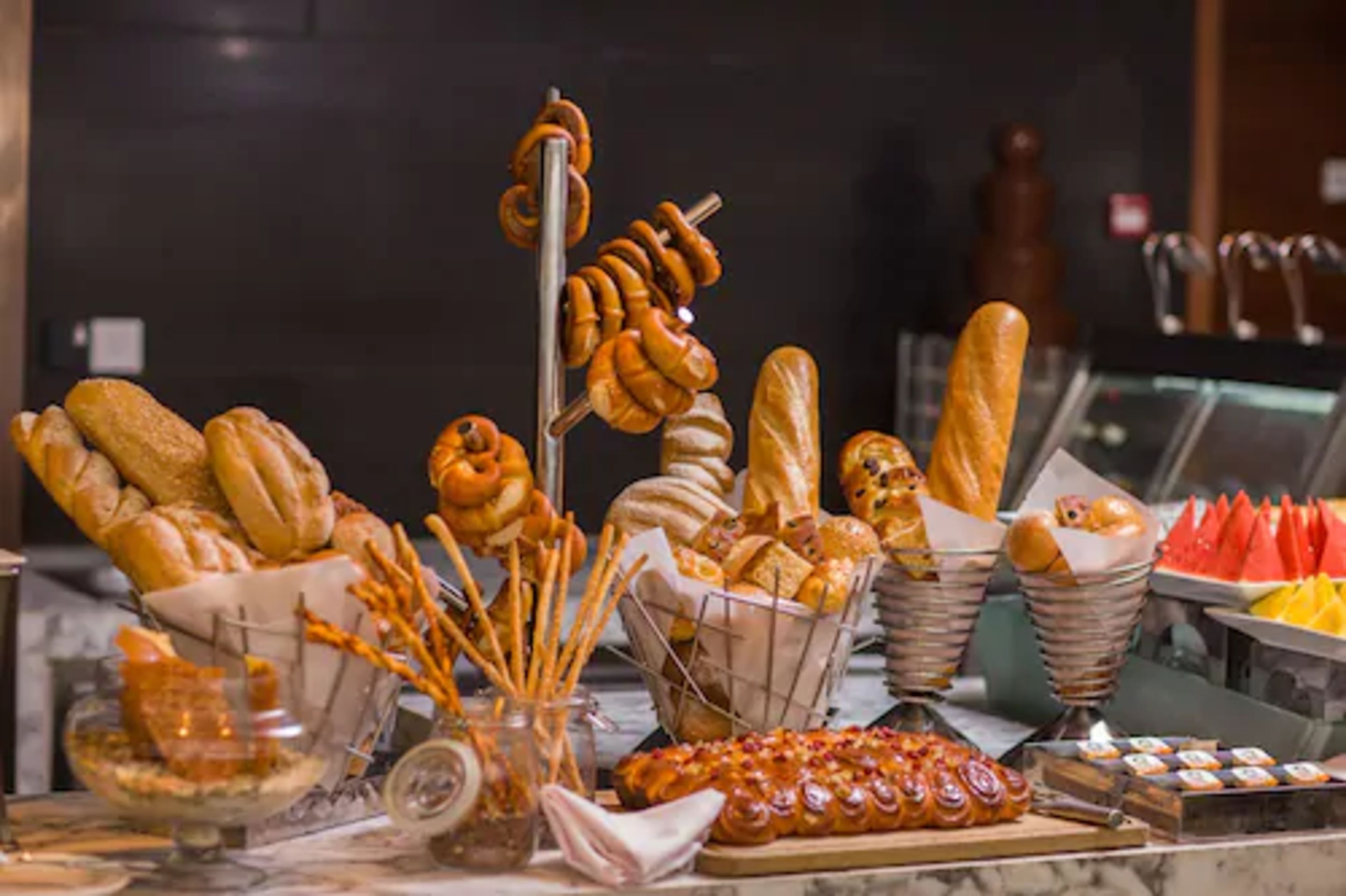 Variedad de productos de panadería, como pan, pretzels y pasteles, expuestos en un bufé.
