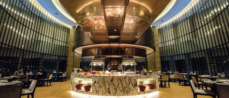 A modern restaurant with a central bar, wooden flooring, and a curved ceiling design.