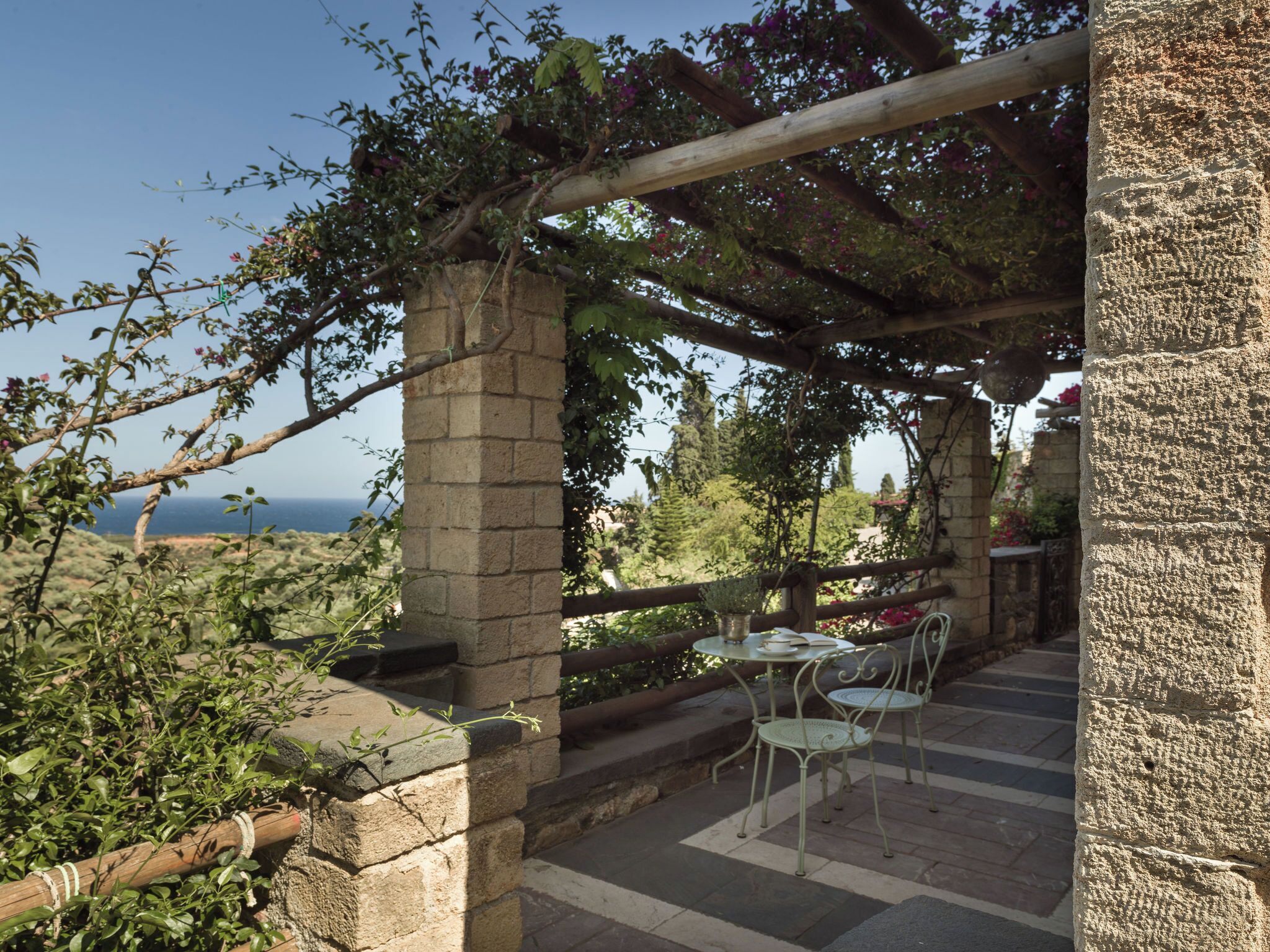 Une pergola en pierre offrant une vue sur la mer, avec des sièges extérieurs et une végétation luxuriante.