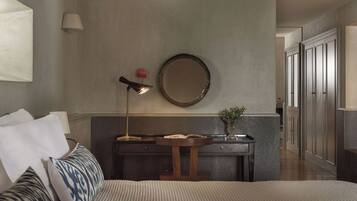 Habitación de hotel con cama, mesita de noche, lámpara, espejo y vista al pasillo.