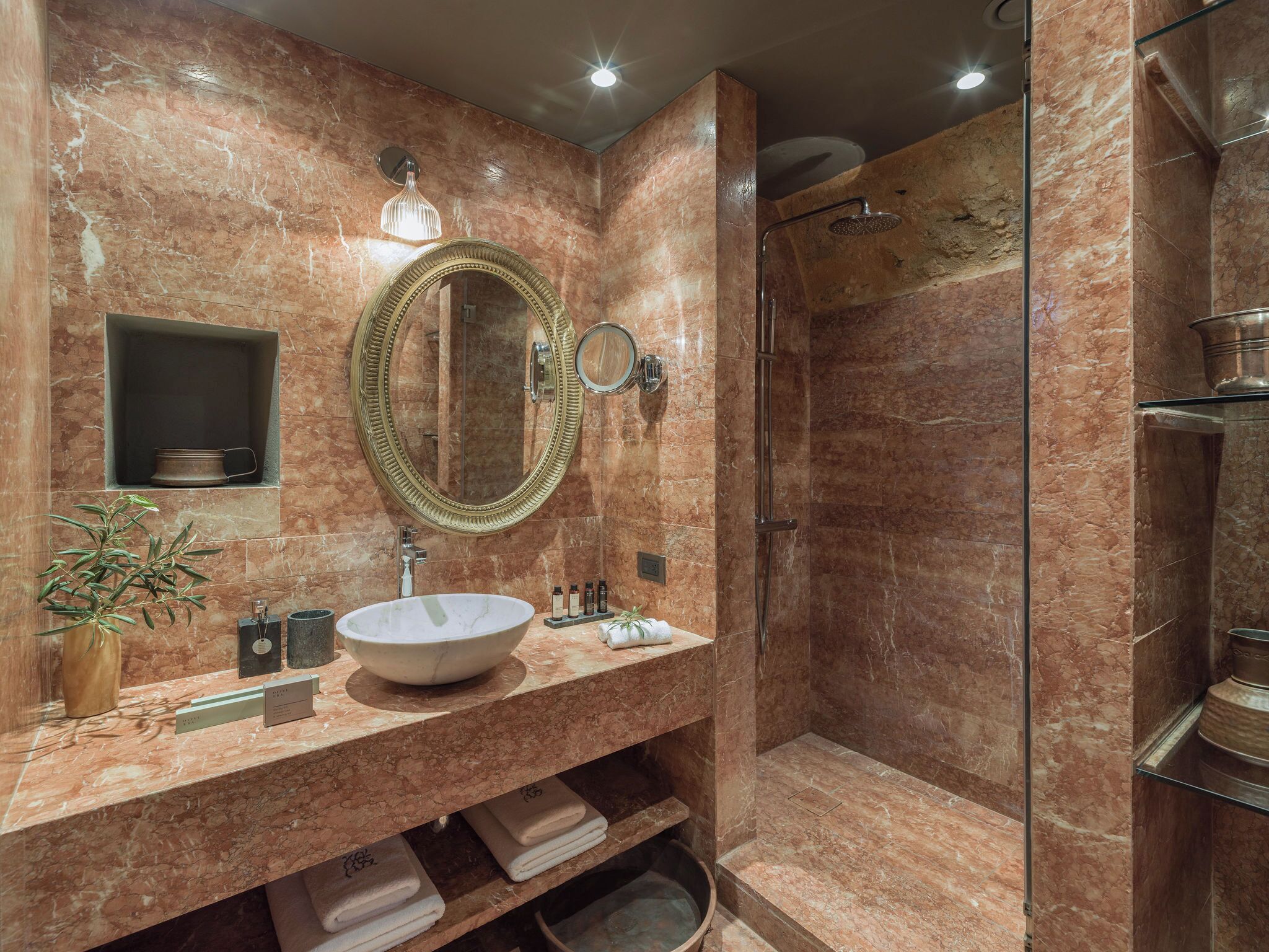 A bathroom with a marble sink, a large mirror, a shower, and a potted plant.