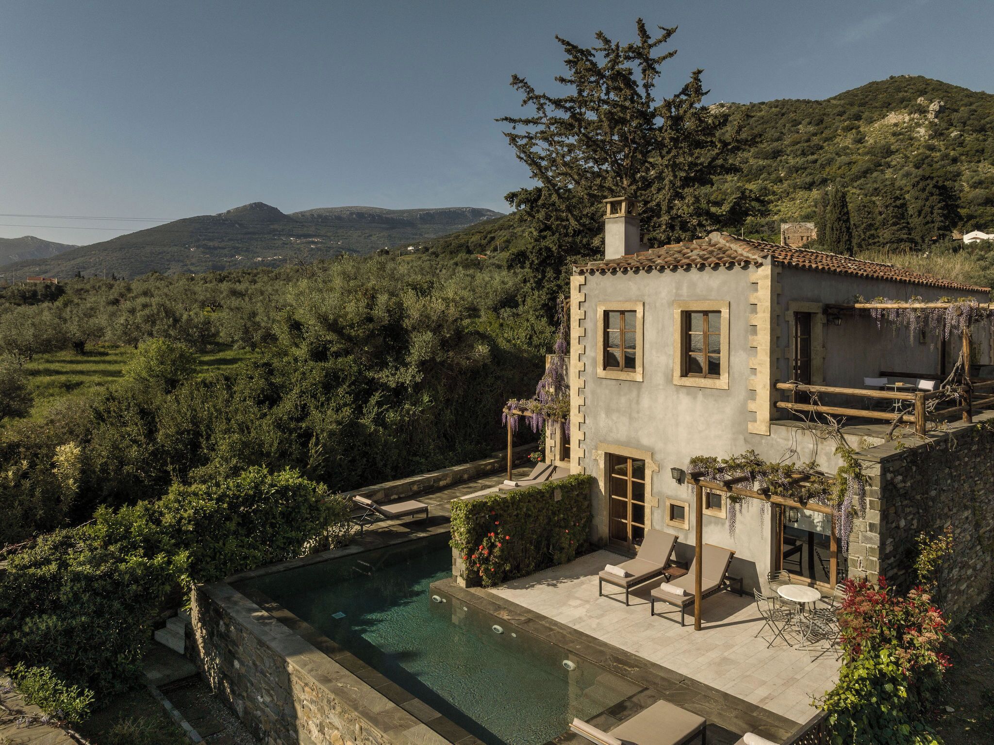 A villa with a swimming pool, outdoor seating, and a view of the surrounding hills.