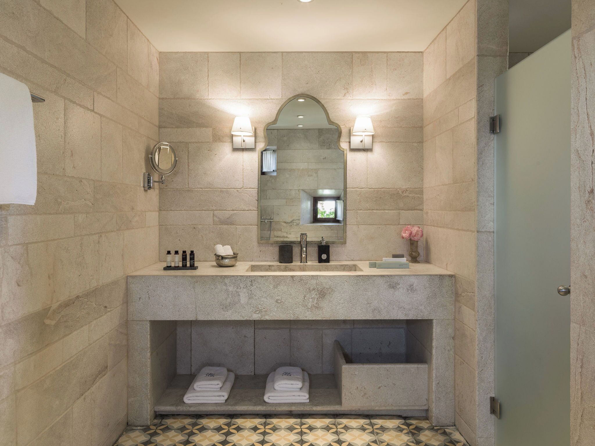 A bathroom with a stone wall, a large mirror, two sinks, and a shower area.