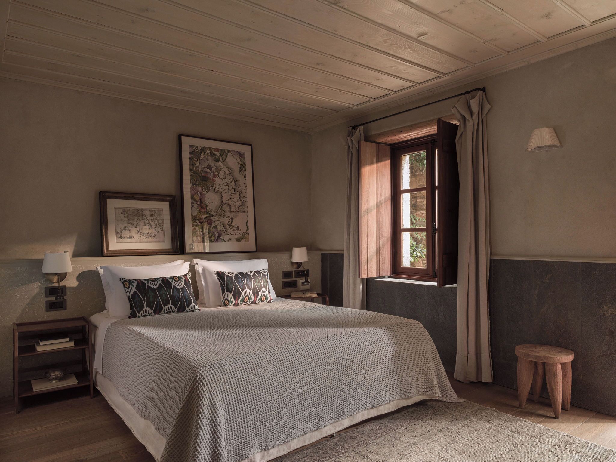 A bedroom with a large bed, two bedside tables, a window with curtains, and a map on the wall.