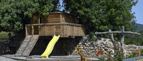 A wooden play structure with a slide, a climbing wall, and a swing set.