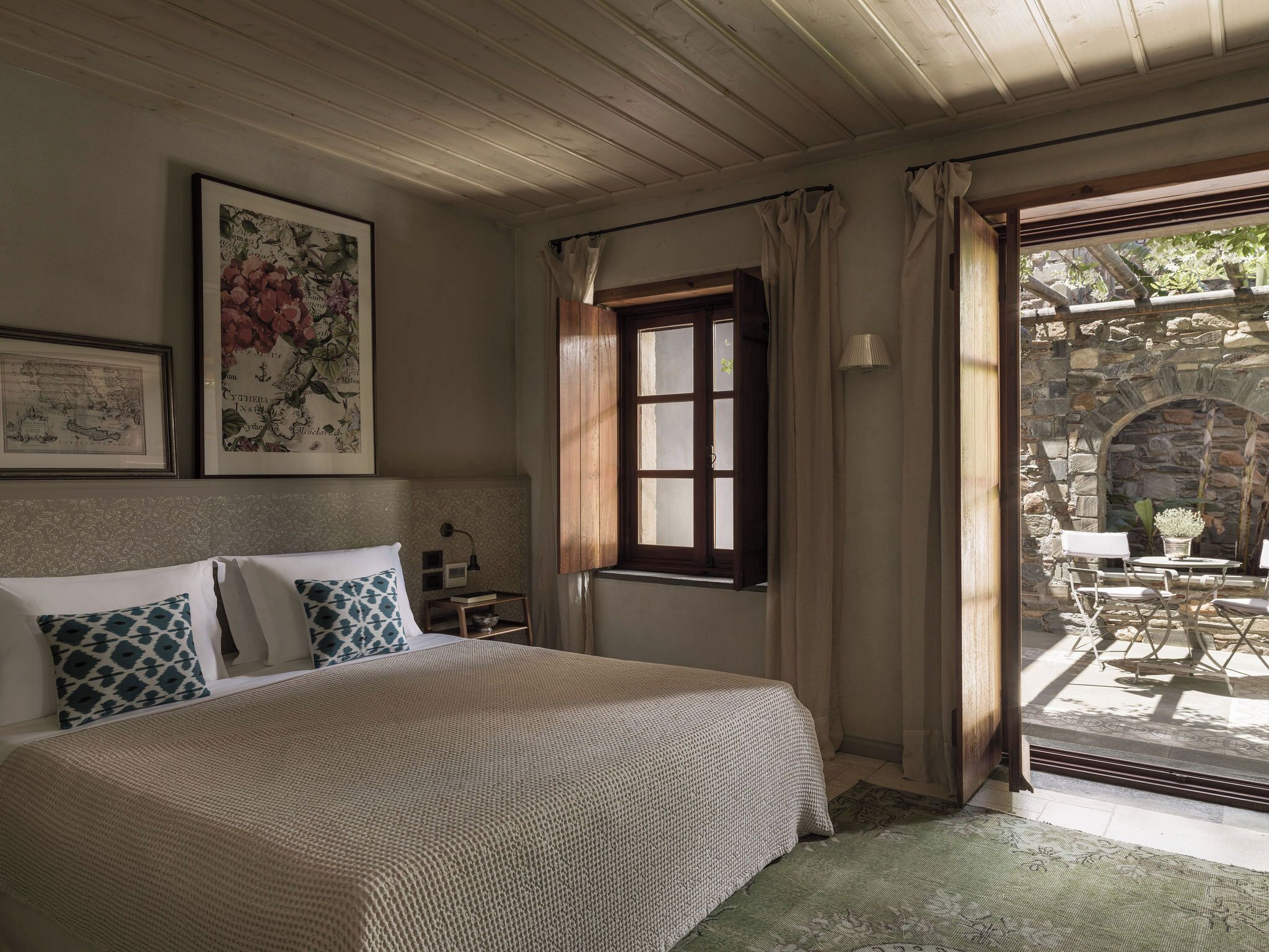 Un dormitorio con cama, mesita de noche, ventana y vistas a un patio exterior.