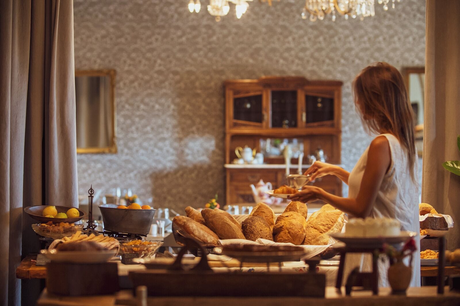 Una mujer sirve comida en una mesa con pan y fruta.