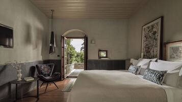 A bedroom with a large bed, a chair, a small table, and a TV on the wall.