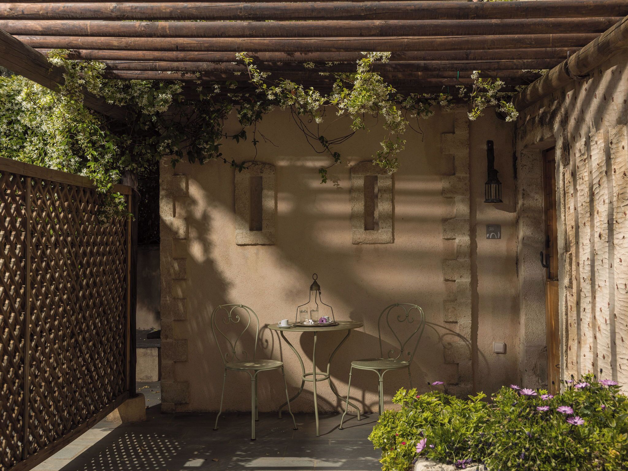 Et hyggeligt udendørs opholdsområde med et pergola, to metalstole og et lille bord.