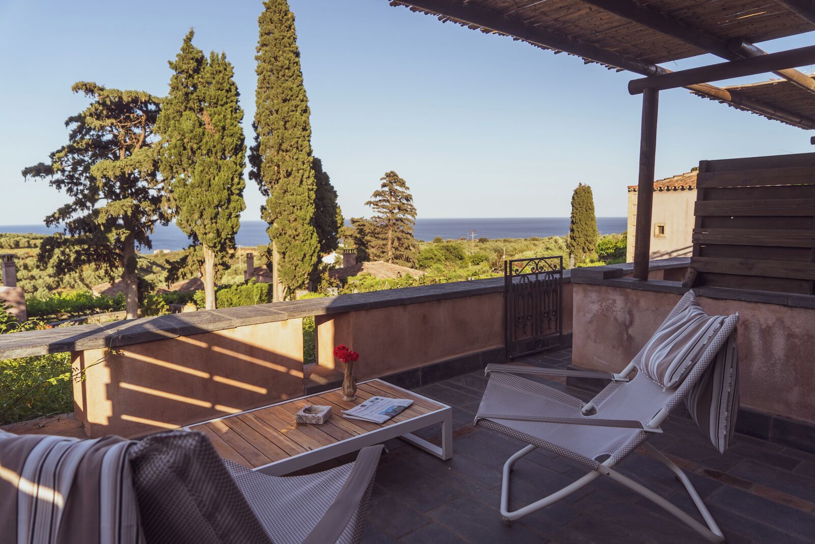Una terraza con dos sillones, una mesa y vistas al mar y a los árboles.