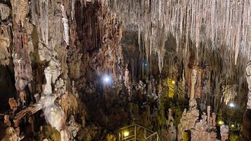 A cave with stalactites and stalagmites, a staircase, and artificial lighting.