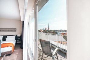 Een hotelkamer met balkon, een bed, een stoel en uitzicht op een stadsbeeld met een kerktoren.