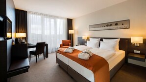 A hotel room with a bed, a desk, a chair, a TV, and a painting on the wall. - Atlantic Hotel Luebeck (Lübeck)