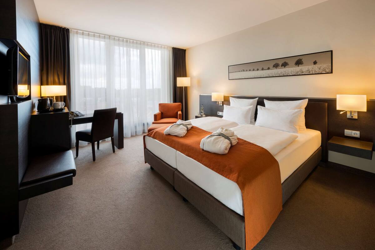 Une chambre d’hôtel avec un lit, un bureau, une chaise, une télévision et un tableau au mur.