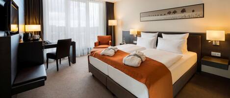 A hotel room with a bed, a desk, a chair, a TV, and a painting on the wall.