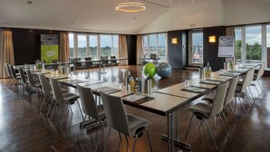 A conference room with a long table, chairs, and a city view through large windows. - Atlantic Hotel Luebeck (Lübeck)