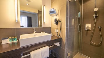 A modern bathroom with a large sink, a mirror, a handheld showerhead, and a glass-enclosed shower.