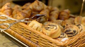 Uma cesta de vime cheia de diversos doces, incluindo croissants e um pão de sementes de papoula.