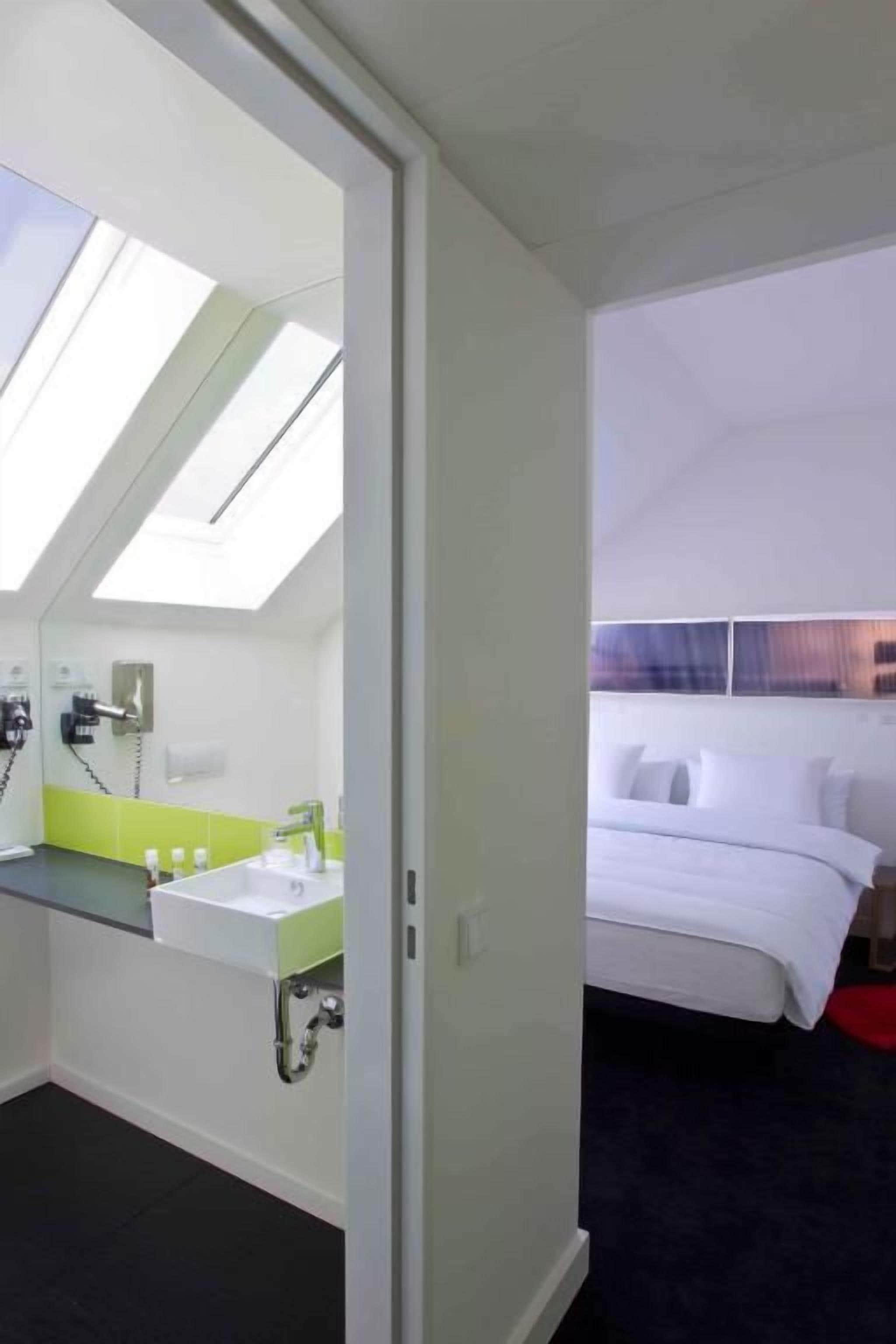 A hotel room with a skylight, a bed, and a bathroom with a green countertop.