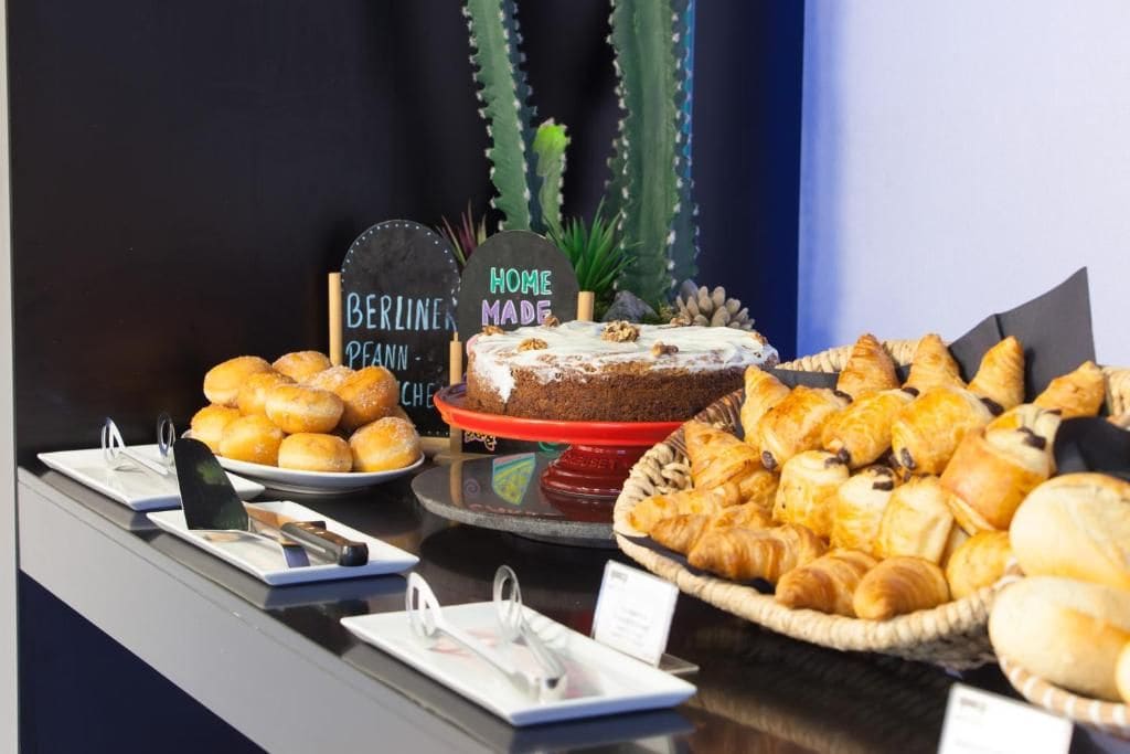 Un bufé con diversas opciones de productos horneados, incluyendo pasteles, tartas y pan, con un letrero que indica 'Home Made' y 'Berlin Made'.