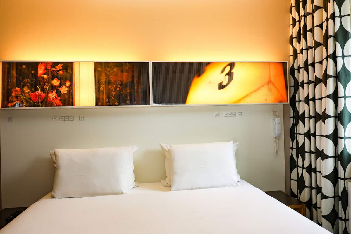 A hotel room with a bed, two pillows, a nightstand, a phone, and a wall with three framed pictures.