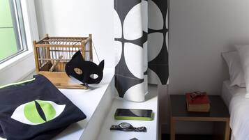 Un dormitorio con cama, mesita de noche, ventana, cuna y pared con un diseño geométrico.