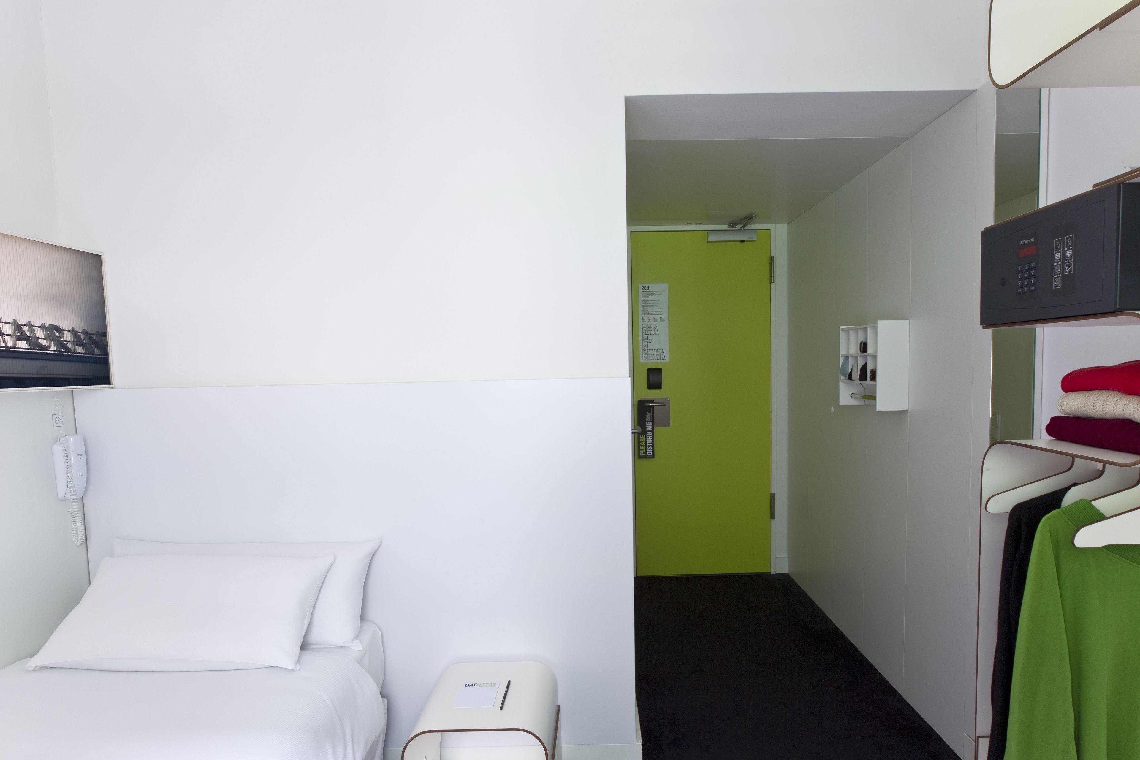 A hotel room with a bed, a small bedside table, a telephone, a green wall, and a clothing rack with towels.
