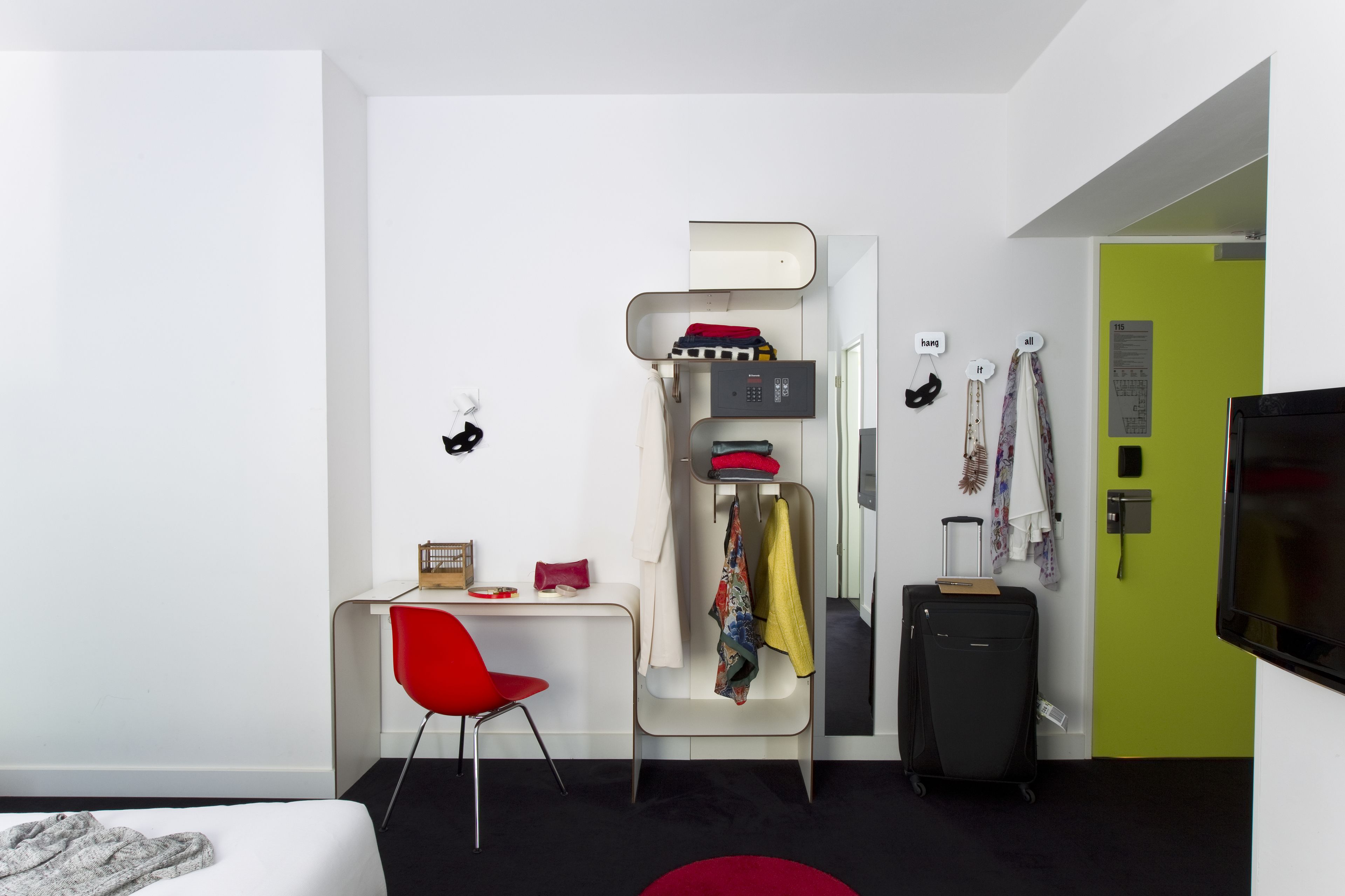 A modern hotel room with a bunk bed, a desk with a chair, a suitcase, and a television.