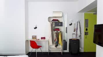 Una habitación de hotel moderna con una cama litera, un escritorio con silla, una maleta y un televisor.