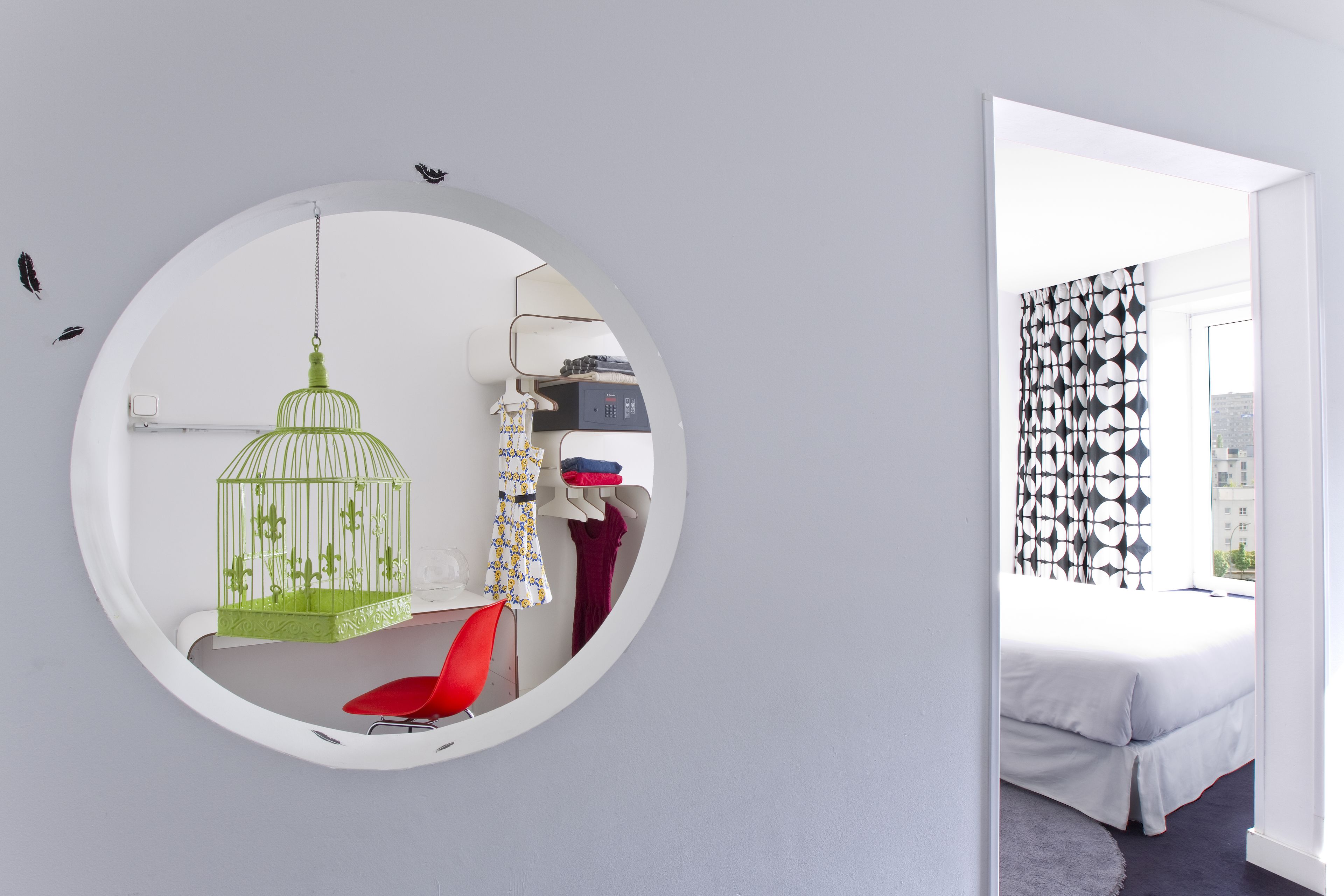 Un espejo circular que refleja una habitación con una cama, una silla roja y una jaula de pájaro verde.