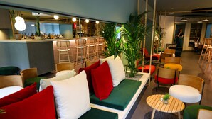 A modern lounge area with a bar, seating with red and green cushions, and a variety of chairs and tables. - Hotel Gat Point Charlie Berlin (Berlin)