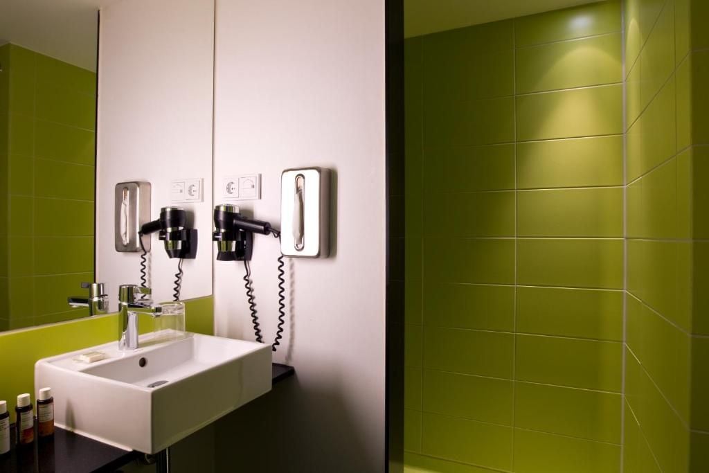 A bathroom with a white sink, a mirror, and two hair dryers mounted on the wall.