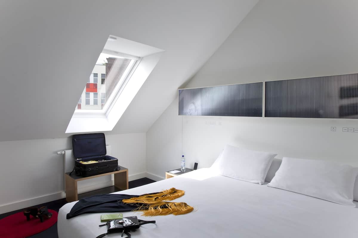 A hotel room with a bed, a skylight, a desk, and a wardrobe.