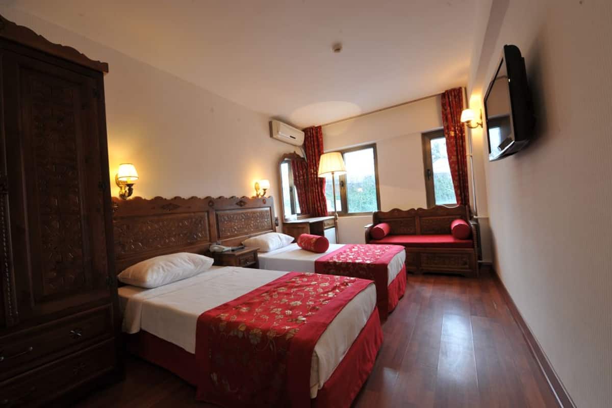 A hotel room with two beds, a wooden wardrobe, a TV mounted on the wall, and a window with curtains.