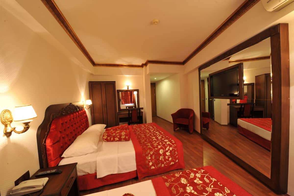 A hotel room with a large bed, a desk with a lamp, a chair, a TV, and a mirror.