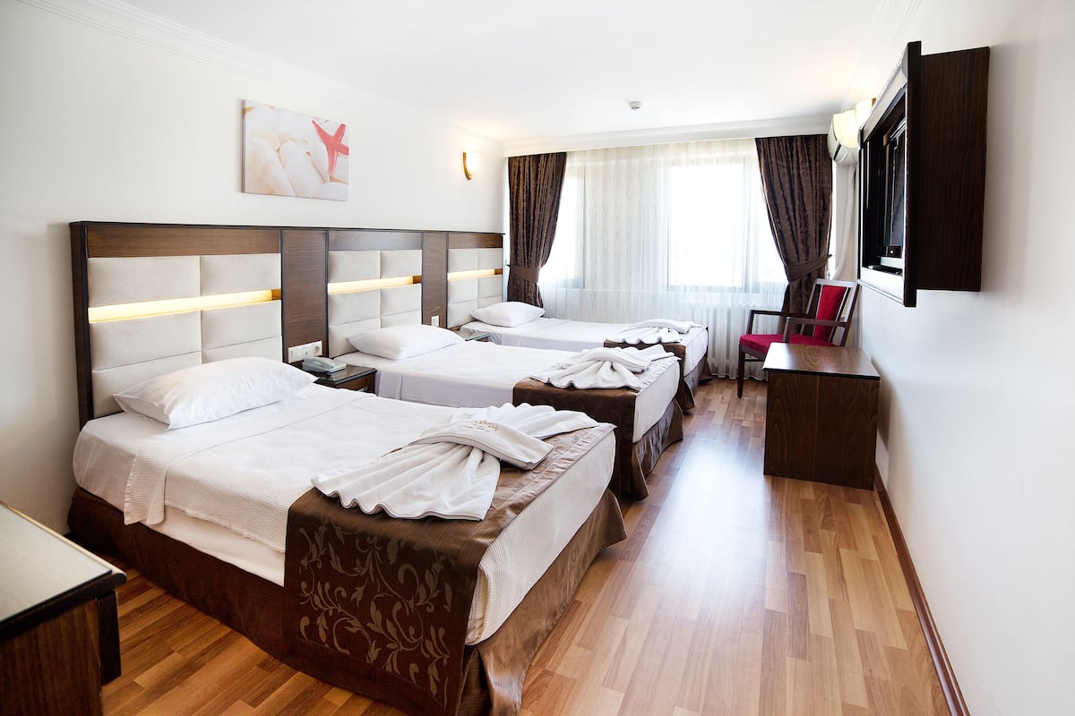 A hotel room with three beds, a desk, and a TV mounted on the wall.