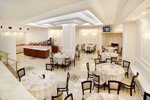 A hotel dining area with multiple round tables and chairs, a reception desk, and a television screen on the wall. - Hotel Santa Pera (Istanbul)