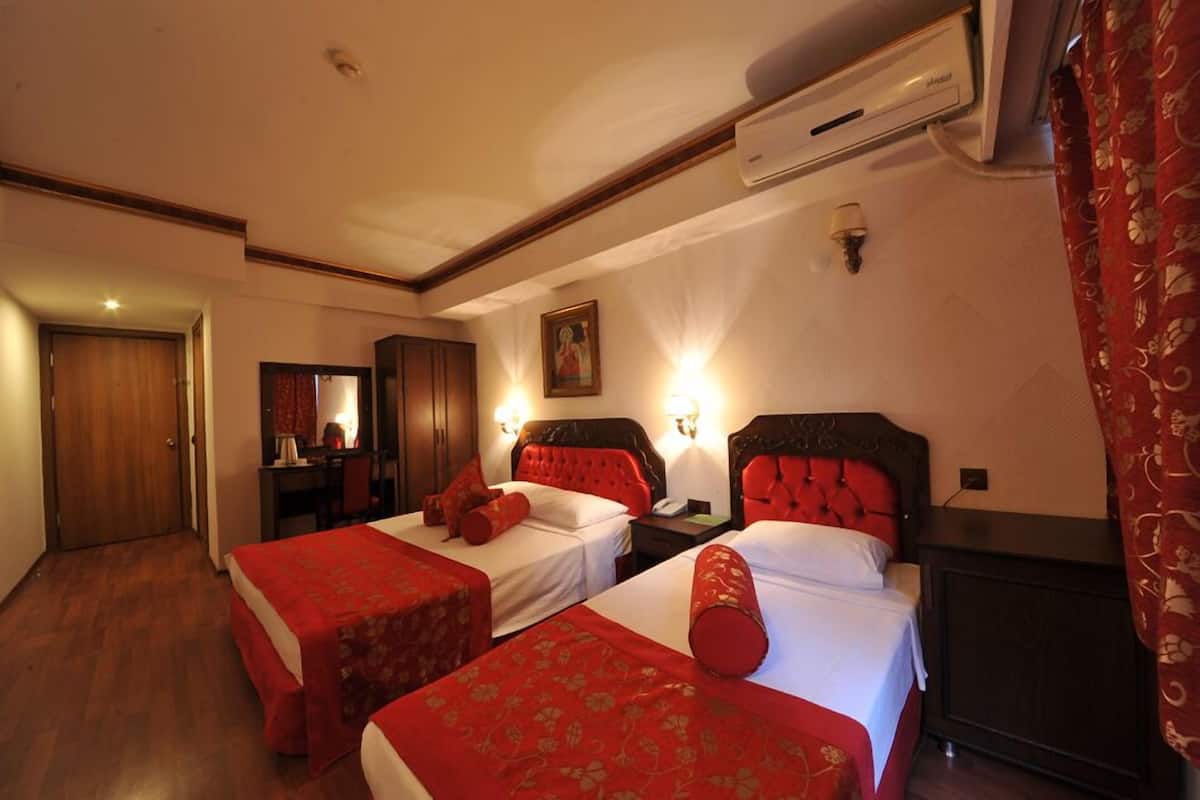 A hotel room with two beds, a desk, a chair, an air conditioning unit, and a mirror.