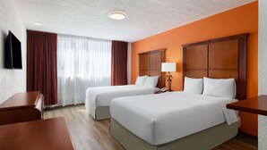 Une chambre d’hôtel avec deux lits, une télévision, un bureau et une fenêtre avec des rideaux.
