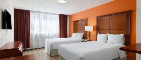 Una habitación de hotel con dos camas, televisión, escritorio y ventana con cortinas.