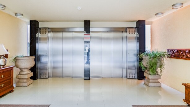 Un espace moderne pour les ascenseurs, agrémenté d’une colonne en marbre, d’une armoire en bois et d’une plante en pot.