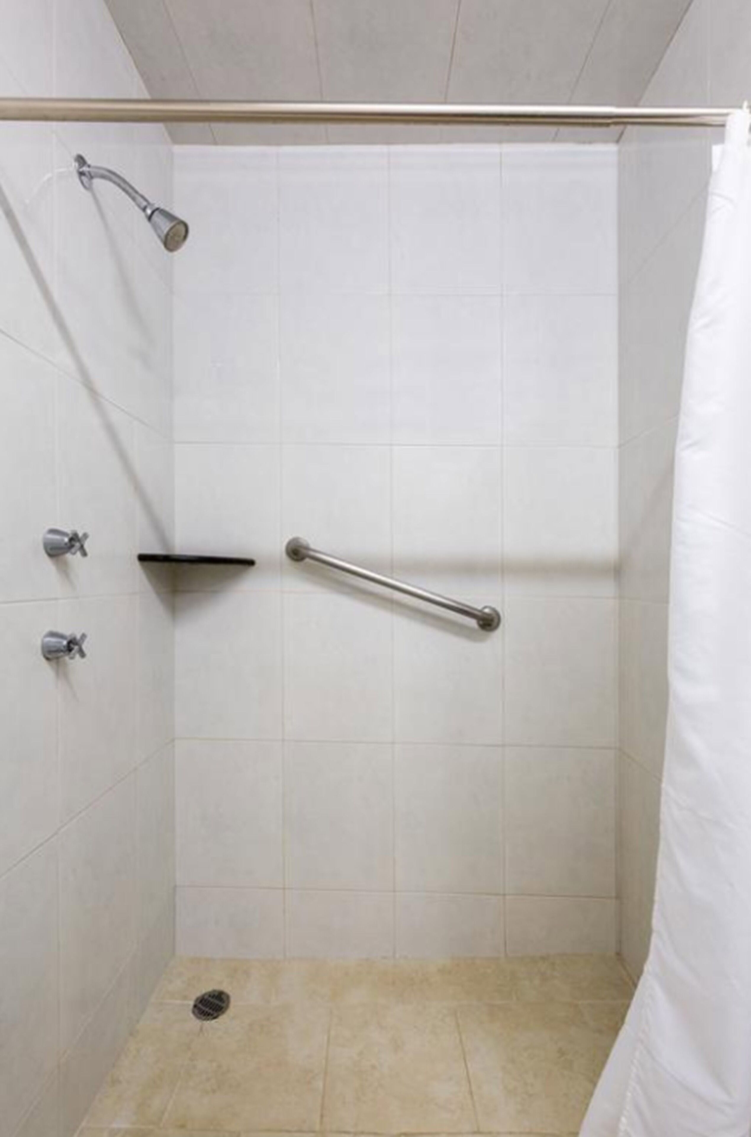 A shower with a grab bar, a showerhead, and a tiled floor.