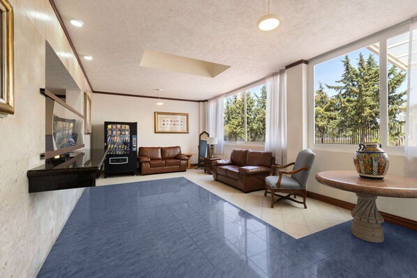 A spacious lobby with a large blue carpet, leather sofas, a coffee machine, and a decorative vase on a table.