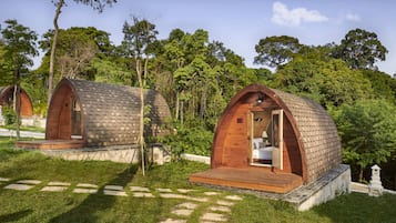 Two wooden dome-shaped cabins with a bed, a small table, and a bench.